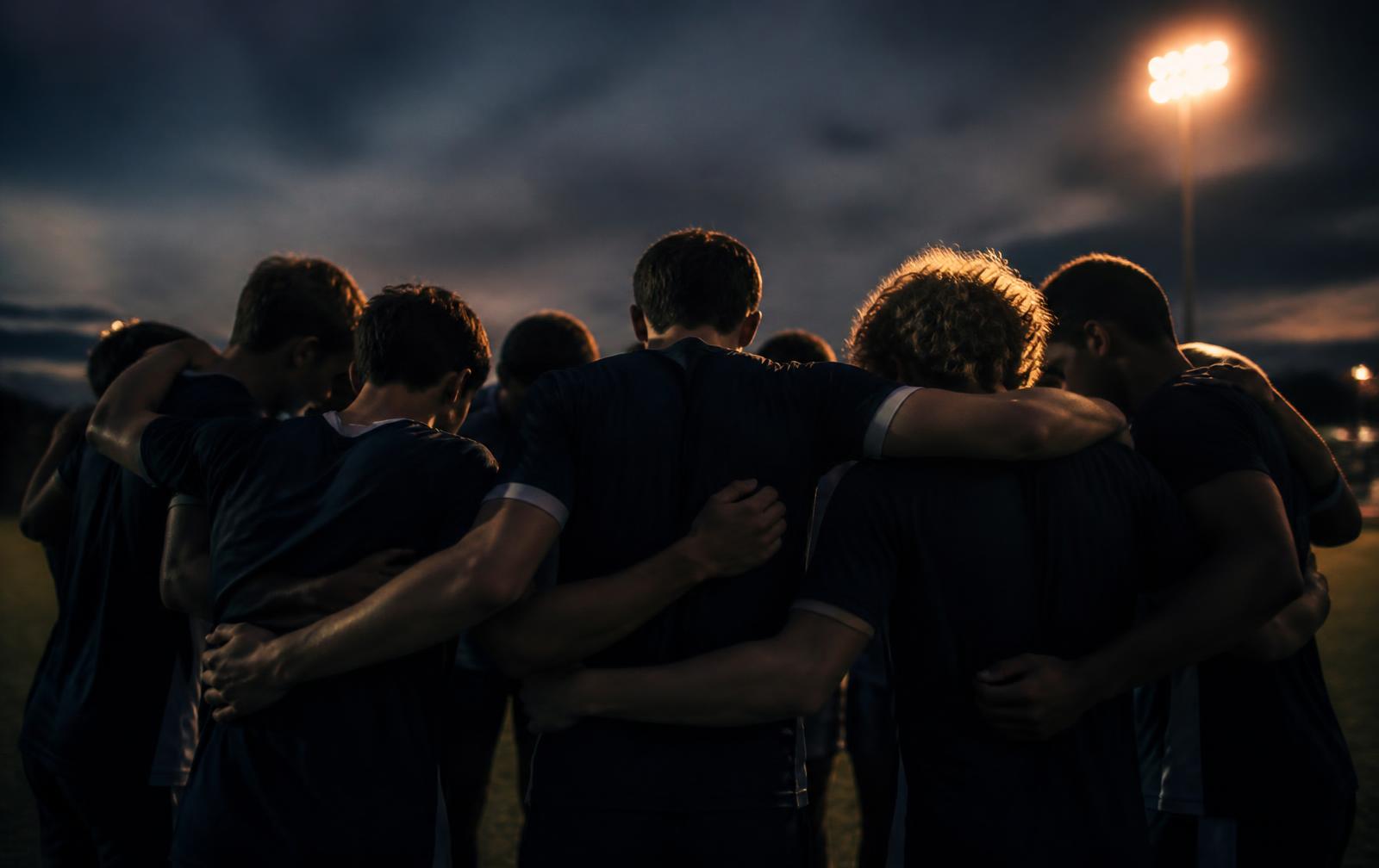 Team huddled together on a field under stadium lights